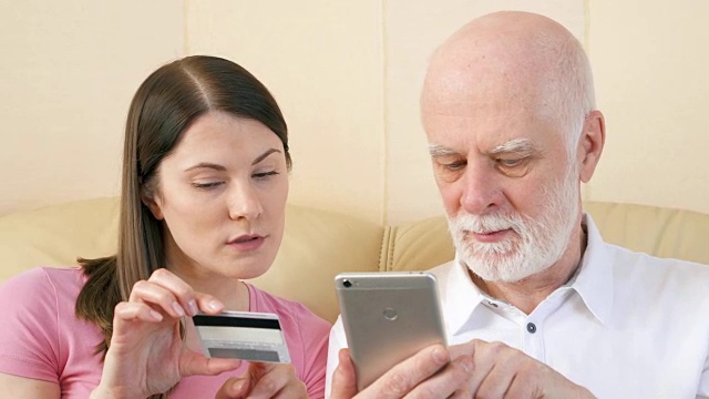 父亲和女儿用智能手机上的信用卡在网上购物。老年人使用的技术视频素材
