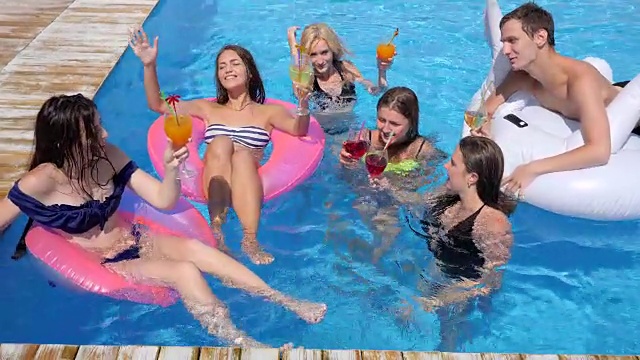 朋友青年游泳在充气环进入游泳池与彩色饮料在夏季假期视频下载