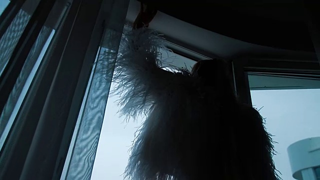 一个女人站在打开窗户的窗台上，抓住他的上衣视频下载