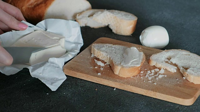 特写的女人用刀把黄油涂在一片面包上。做一个三明治。视频下载