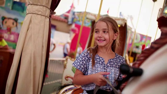 年轻的女孩骑着旋转木马在旋转木马上视频素材