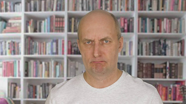 肖像愤怒的人的脸看着相机在书柜的背景视频素材