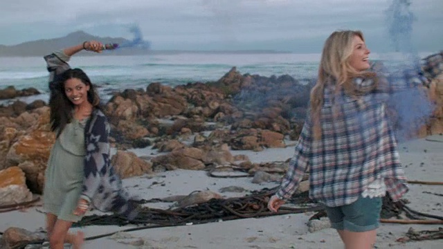 两名年轻女子在海滩上拿着彩色烟雾弹视频素材