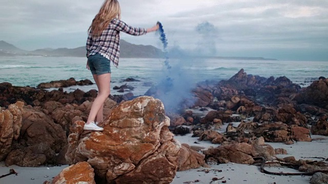 一个女人在海滩的岩石上拿着烟雾弹视频素材