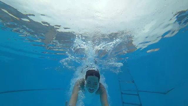 女孩睁着眼睛跳入水中，慢镜头中她漂浮在蓝色的泳池边视频素材