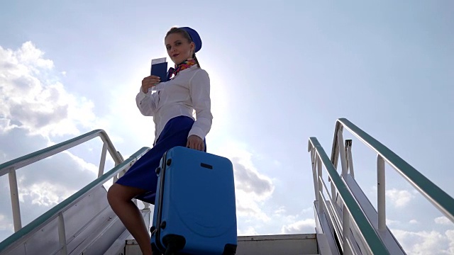 在机场的飞机楼梯上，空姐在背光下拿着行李箱和护照视频下载