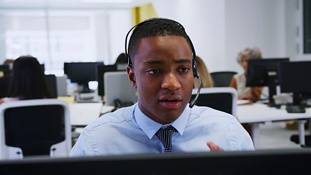 在繁忙的办公室里戴着耳机在电脑前工作的年轻人视频素材