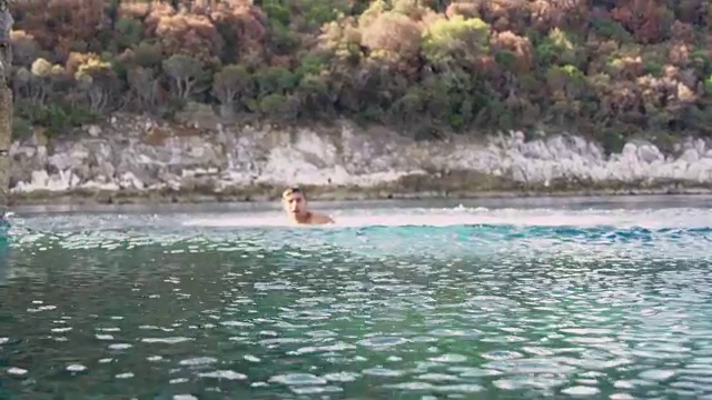 4K好玩的男人跳进阳光明媚的夏日海洋，慢镜头视频素材