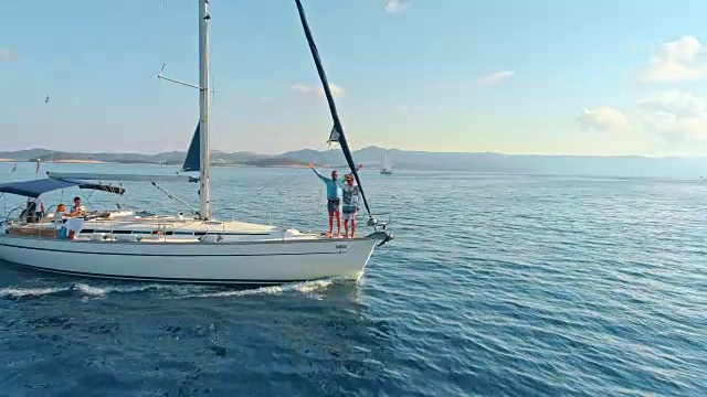 4K无人机视角下的朋友在宁静、阳光明媚的蓝色海洋上的帆船上，实时视频素材