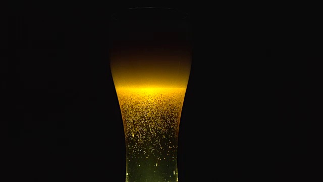 将冰镇啤酒倒入有水滴的玻璃杯中。视频素材