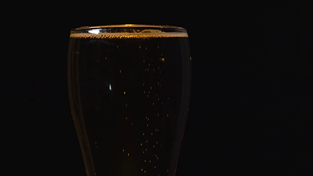 在黑色背景上的一个玻璃杯里的冷光啤酒。精酿啤酒近距离。一品脱的啤酒。视频素材