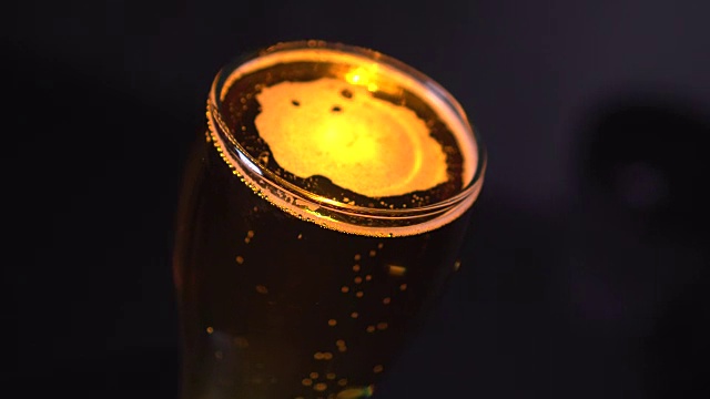 冷光啤酒在一个玻璃孤立的黑色背景。精酿啤酒近距离。旋转360度。视频素材