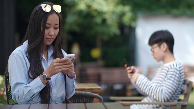 亚洲女孩在户外咖啡馆用智能手机打字视频素材
