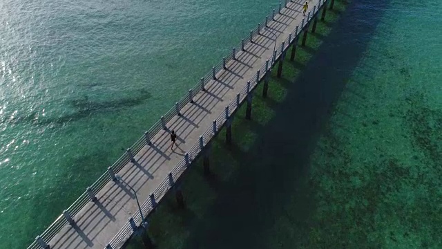 那个穿黑衣服的女孩正沿着海边的桥跑。视频素材