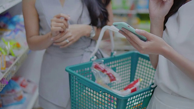 两名年轻女子在超市购物并使用智能手机视频购买