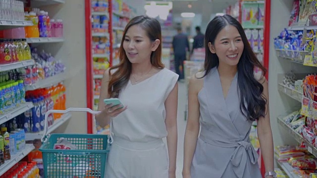 两名年轻女子在超市里用智能手机购物，慢镜头视频素材