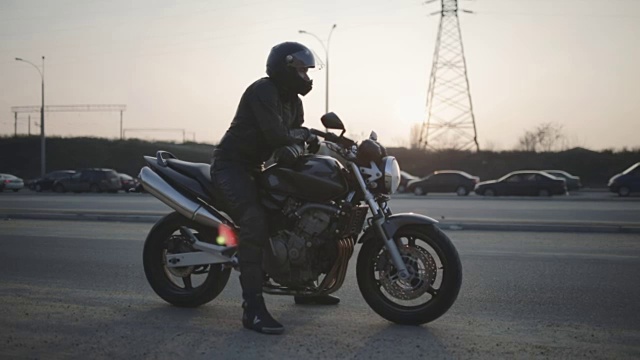 年轻迷人的摩托车手戴着黑色头盔在街上。男人摩托车骑士视频素材