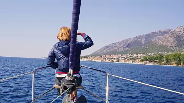 在克罗地亚布拉克岛的Bol沿岸阳光明媚、宁静的海洋上，一位女士坐在帆船的船头视频下载