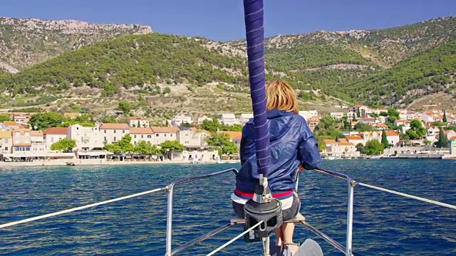 克罗地亚布拉克岛，一名女子站在帆船船头，看着阳光明媚的波尔视频下载