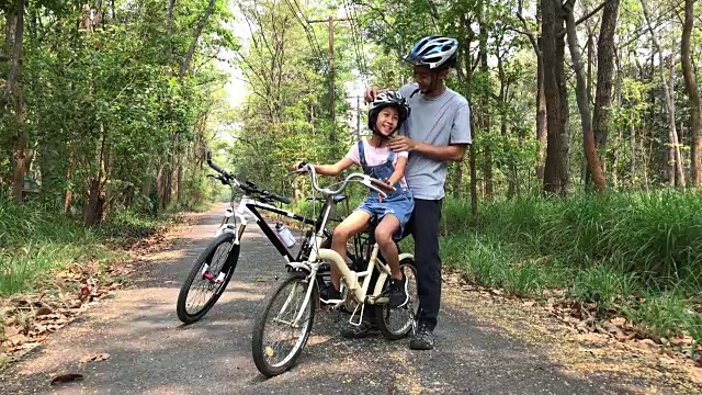 快乐的爸爸和女儿在公园里骑着自行车头盔给女儿看视频素材