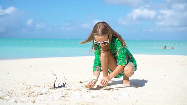 热带海滩上，一个手里拿着贝壳的可爱小女孩。可爱的小女孩在海滩上玩贝壳视频素材