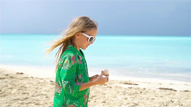 热带海滩上，一个手里拿着贝壳的可爱小女孩。可爱的小女孩在海滩上玩贝壳视频素材