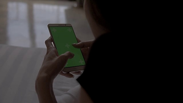 亚洲女子在床上拿着绿色屏幕的手机视频下载