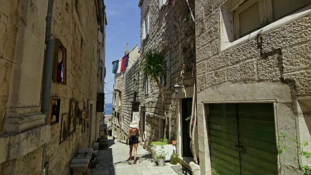 克罗地亚科尔库拉岛，女游客走在阳光明媚的小巷里视频下载