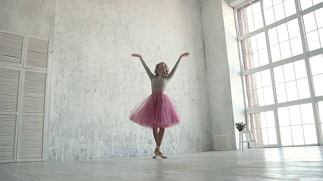 一名优雅的年轻芭蕾舞演员穿着经典的芭蕾舞短裙，在一扇大窗户的背景下指指点点视频素材
