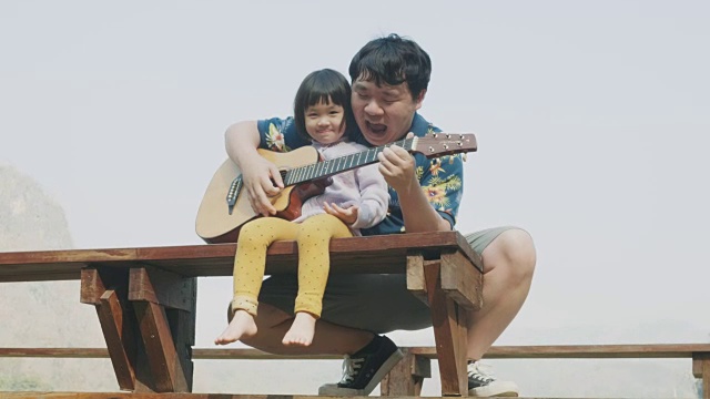 一位亚洲父亲在阳台上教女儿弹吉他视频购买