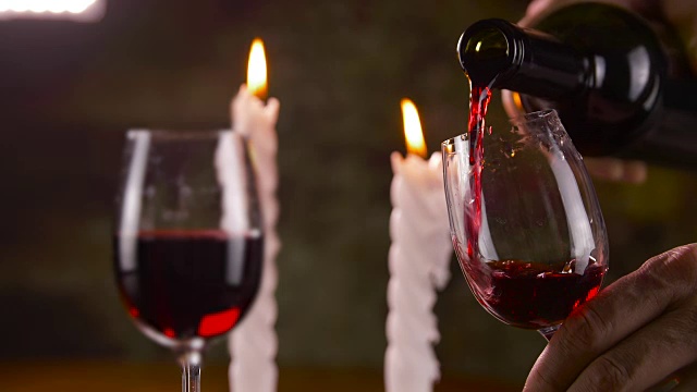 在蜡烛的背景上，用手将红酒倒入玻璃杯中视频素材