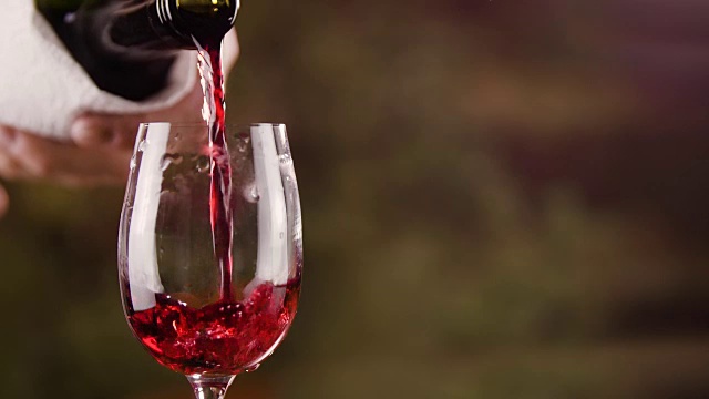靠近男性的手倒红酒在玻璃从瓶子缓慢的动作视频素材