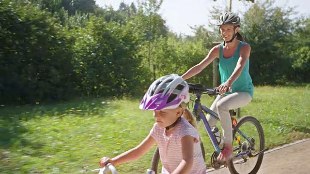 一个小女孩和她的妈妈在一个阳光明媚的公园里骑车视频素材