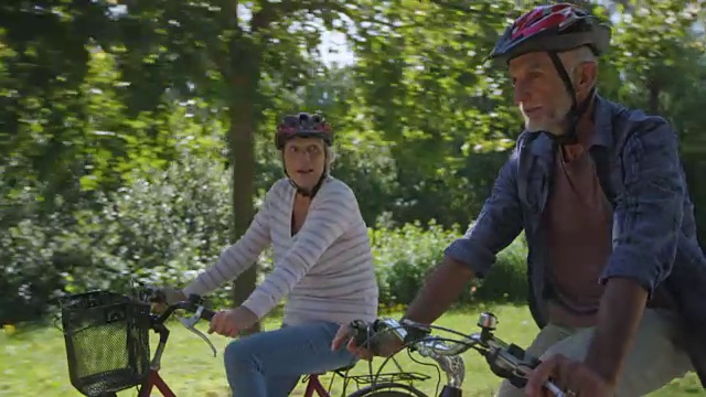 在阳光明媚的公园里，骑着自行车的老男人和女人在交谈视频素材