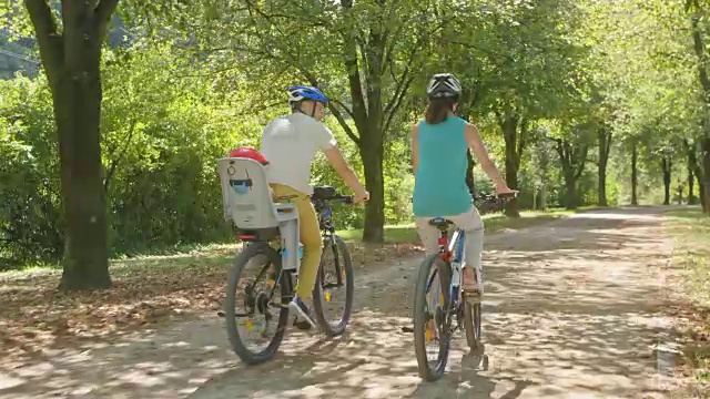 一对夫妇在阳光明媚的公园里骑车，他们的孩子坐在自行车的儿童座椅上视频素材