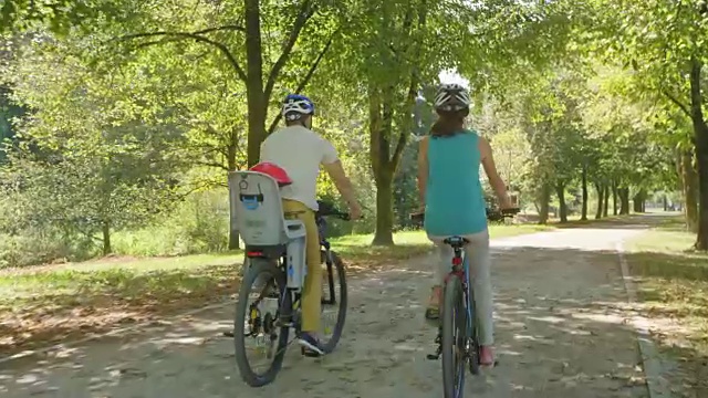 丈夫和妻子在一个阳光明媚的日子里带着他们的孩子在公园里骑车视频素材
