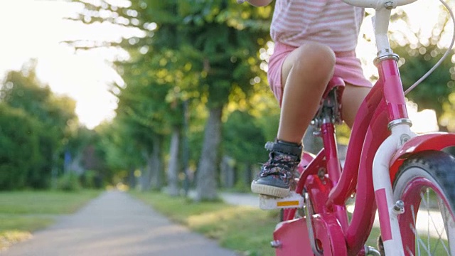阳光下的郊区，一个小女孩在推着她的自行车踏板视频素材
