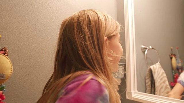一个掉了牙的小女孩看着浴室的镜子，然后对着镜头微笑视频素材