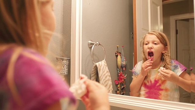 一个掉了一颗牙的小女孩，把卫生纸放到嘴边，看着镜子视频素材
