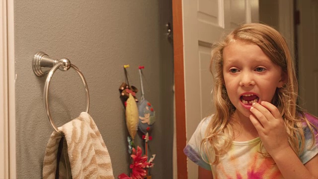 一个小女孩掉了一颗牙后，在浴室的镜子里晃动着一颗松动的牙齿视频素材