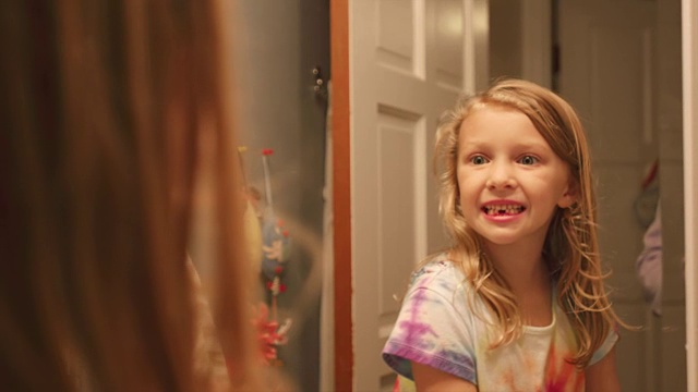 一个小女孩拿起她刚掉的两颗牙，微笑着对着镜子做鬼脸视频素材