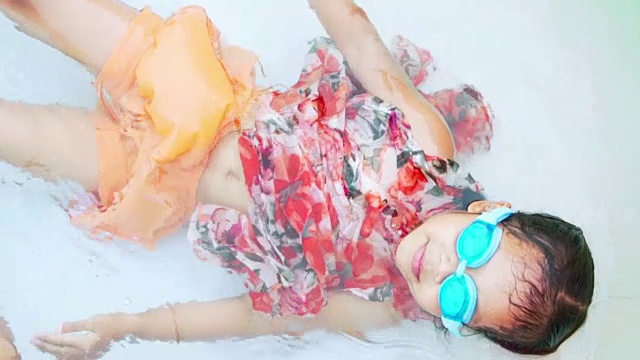 可爱的亚洲儿童女孩戴着泳镜游泳和躺在橡胶游泳池与乐趣在夏季时间在慢动作拍摄视频下载