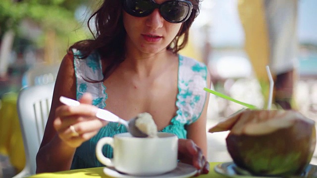 漂亮的女孩戴着太阳镜在海滩咖啡馆吃早餐燕麦片。1920 x1080视频下载