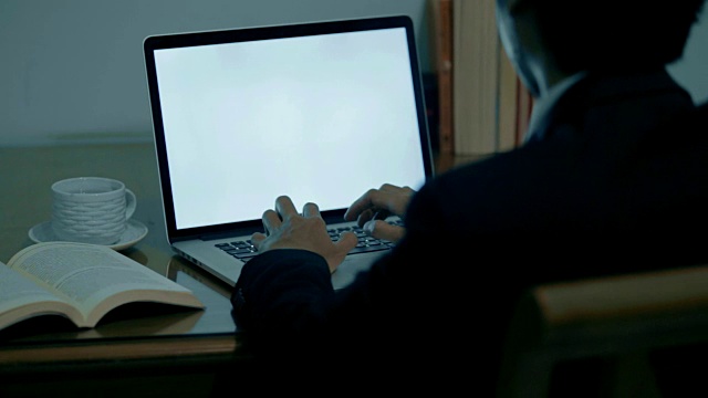 一个人坐在他的桌子和打字的笔记本电脑上的白色屏幕在家里/办公室有两种色调视频下载