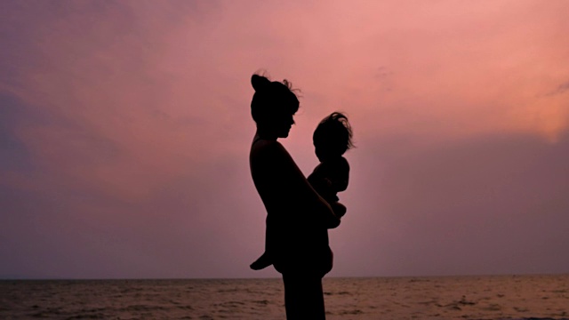 年轻的母亲抱着孩子在海滩剪影视频素材