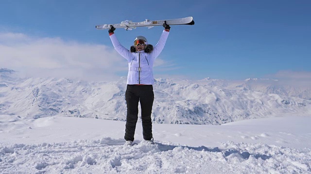 女子滑雪者站在山坡上，举起滑雪板，挥动4K视频素材