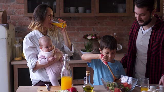 父亲和儿子煮沙拉，母亲喝果汁和抱着婴儿视频素材