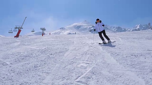在运动中，一个女滑雪者从山上的滑雪坡上雕刻下来视频素材