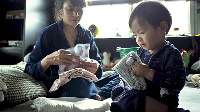 亚洲妇女折叠衣服看顽皮的小男孩玩。视频下载