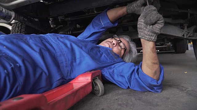 摄影车从他的脚上拍摄:亚洲高级汽车技师躺在车下工作视频素材